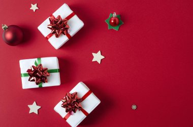 Kırmızı ve yeşil kurdelelerle bembeyaz kağıda sarılmış hediyeler, kopyalama alanı olan parlak kırmızı dikey bir zemin üzerinde yatar.