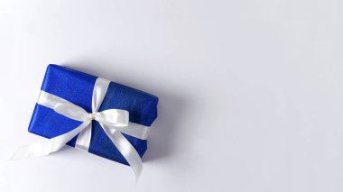 Gift box in blue paper with white ribbon on a white background. Gift concept for New Year, Christmas, Valentine's day, congratulations with copy space and flat lay clipart