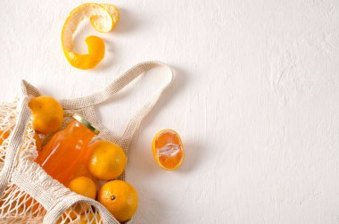Drink from tangerines in a bottle and tangerines fruits lie in a net bag on a light background with copy space, selective focus, horizontal background