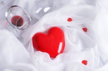 Kırmızı bir kalp, beyaz, havadar bir kumaşa sarılı bir şarap kadehiyle. Kopya alanı ile Sevgililer Günü konsepti