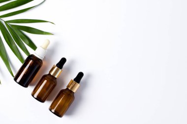 Koyu cam şişelerde serum, beyaz zemin üzerinde kozmetik yağ palmiye yaprağı, düz uzanma, yatay görüntü, kopyalama alanı