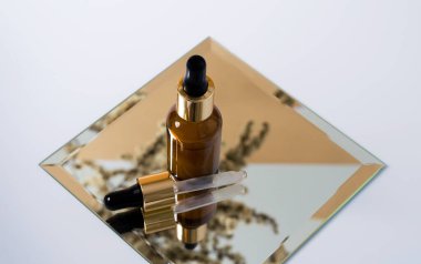 Kahverengi bir şişede pipetle serum aynada duruyor ve aynadaki yansıması beyaz bir arka planda. Doğal yağlarla kaplıca kavramı, kopyalama alanı ile