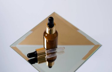 Şişede pipetli bir yüzle ilgilenmenin anlamı, yansıması olan kare bir aynanın üzerinde duruyor, yanında bir pipet, açık bir arkaplan.