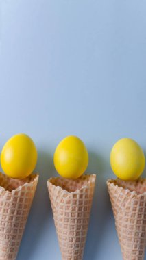 Üç waffle külahı dikey mavi arkaplanda yatar, yakınlarda sarı boyanmış yumurtalar, paskalya arkaplanı konsepti, seçici odak, düz alan, kopyalama alanı