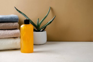 Şampuan, jöle, şeffaf bir şişedeki doğal malzemelerden yapılmış turuncu sıvı sabun bej bir arka planda duruyor. Bir yığın bej havlunun yanında.