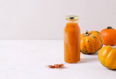 Cam bir kaptaki balkabağından çıkan sebze suyu bej bir arka planda duruyor. Yakınlarda uzayın bir kopyasına sahip turuncu balkabakları var.