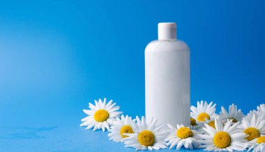 Şampuan, duş jeli, beyaz sıvı sabun. Mavi arka planda, şeffaf bir şişede doğal malzemeler var.