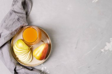 Fruit juice in a transparent glass on a ceramic plate and a concrete background, near a gray napkin and pears, flat lay, copy space