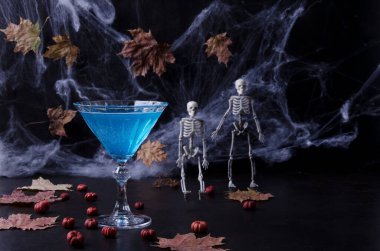 Cadılar Bayramı kokteyli. Kutlama içkisi. Cadılar Bayramı partisi. Balkabakları, örümcek ağları, koyu tonlu arka planda kara bir anahtardaki iskeletler. Seçici odak