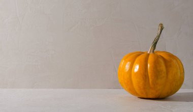 Minimalizm sonbahar arkaplanı - bej arka planda turuncu balkabağı. Metin kopyalama içeren içecek, yiyecek ve ürünlerin gösterimi için boş arkaplan.