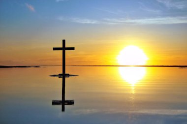 Sahilde karanlık bir haç ve arkasında harika bir günbatımı gökyüzü var. Aynı zamanda düz yansıtıcı su..