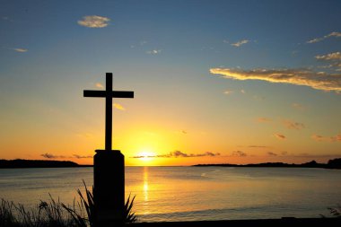 Parlak, sıcak bir günbatımı gökyüzü ve nehir körfezinde bir haçın arkasındaki yansıma..