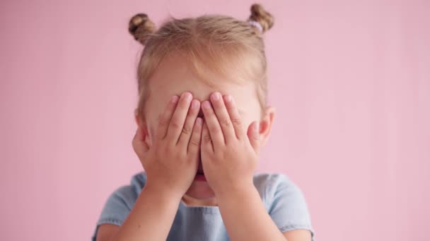 Barndom, fest, födelsedag, spel koncept - närbild liten blond flicka spelar peekaboo tittar på kameran täcker ögon och mun med händer och visar olika känslor på rosa fast bakgrund — Stockvideo
