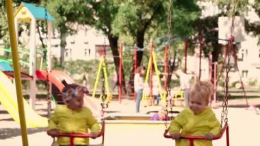 Çocukluk, oyun, eğlence, dostluk, yaşam tarzı konsepti - sarı ceketli iki çocuğun genel planı 2 ve 3 yaşındaki sevimli gülümseme salıncakta salıncakta sallanıyor.