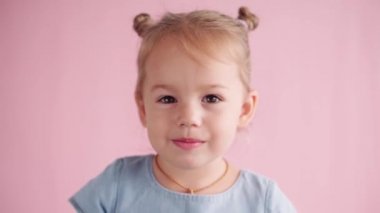 çocukluk, kutlama, doğum günü, oyun konsepti - yakın plan mutlu, mavi elbiseli küçük kız kameraya bakıyor kulakları kapatıyor çığlıklar ve pembe arka planda farklı duygular gösteriyor.