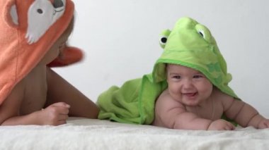 Çocukluk, günlük rutin, hijyen kavramları, banyo yaptıktan sonra beyaz arka planda bornozlu iki mutlu çocuk. Kız ve yeni doğan bebek duştan sonra karın üstü yatıyorlar. Yatmadan önce havlusu olan İrlandalı ikizler.