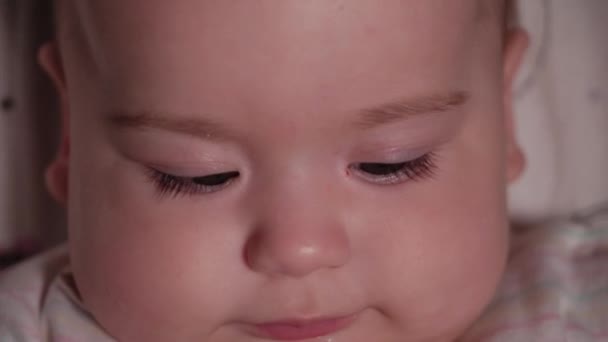 Kojenec, dětství, emoční koncept - Extrémní detailní záběr usmívající se tváře hnědookého novorozence bdělého bezzubé dítě 7 měsíců staré pít vodu z láhve s bradavkou ležící v bílém obleku v kočárku — Stock video