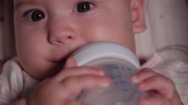 bebek, çocukluk, duygu konsepti - Kahverengi gözlü, yeni doğmuş, dişsiz bir bebeğin aşırı yakın plan gülümsemesi 7 aylık şişeden su içmesi ve bebek arabasında beyaz bir vücut giysisi içinde yatması