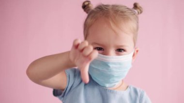 Karantina, covid-19, çocukluk, mesafe ve çevrimiçi öğrenme, okul konsepti - küçük üzgün kızın mavi tıbbi maskeyi çıkarması, parlak pembe arka planda negatif duygu göstergesidir.