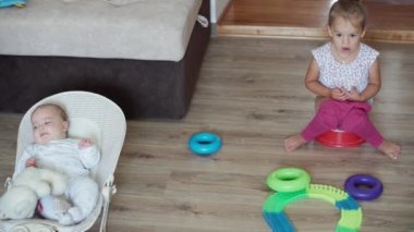 Çocukluk, oyunlar, terbiye ve gelişim konsepti. Rock koltuğunda yeni doğmuş bir bebeğin ve çocuk oyun odasındaki bir tencerede oturan bir kız kardeşin en iyi görünümü. Kardeşler evlerinde eğleniyor.