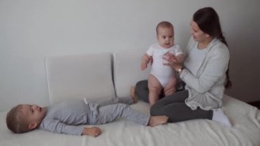 Aile, çocukluk, bebek konseptleri yeni doğmuş bebekli iki çocuk, annemle yatakta zıplıyorlar. Kardeşler küçük erkek ve kız kardeşler evde karantinada eğleniyor ve gülüyorlar..