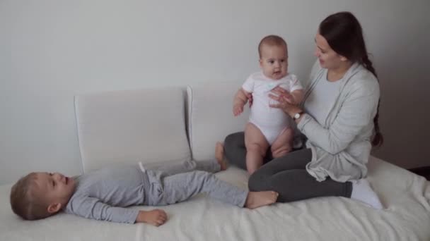 Family, childhood, infant concepts - Two children with newborn baby jumping with mom on bed. Siblings little boy and girl brother and sister have fun and laughing, happy kids on quarantine at home. — Stock Video