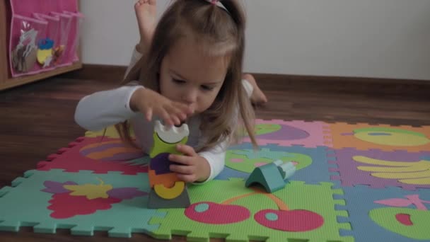 Childhood, family, insulation concept - One cute small happy child build wooden pyramid sitting on floor colored soft mat puzzle. kid girl playing alone educational games for motor skills at home. — Stock Video