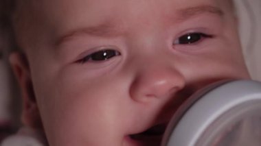 bebek, çocukluk, duygu konsepti - Kahverengi gözlü, yeni doğmuş, dişsiz bir bebeğin aşırı yakın plan gülümsemesi 7 aylık şişeden su içmesi ve bebek arabasında beyaz bir vücut giysisi içinde yatması