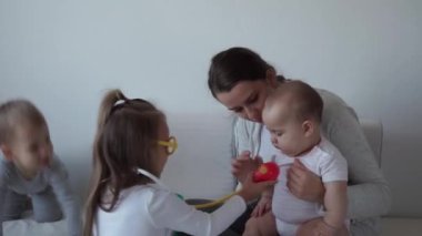 Tıp, aile, oyun konseptleri, konsantre oyun oynayan çocuklar tıbbi gözlük takıyor. Doktor gibi davran, hemşire ol, dinle gülümse anne yeni doğmuş bebek kız kardeşin derin nefes al, yatağa otur.