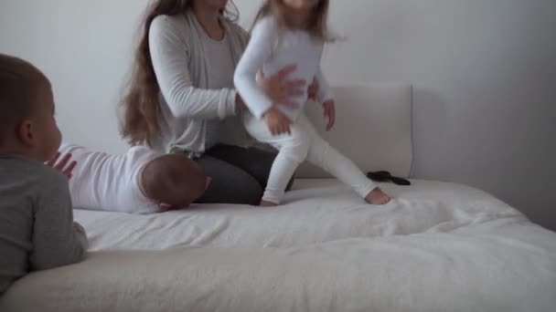 Childhood, motherhood, siblings concept - Carefree young mum combs her little kid daughter hair , son and newborn baby have fun play on bed, happy cheerful family laugh tickles, kiss, hugs lying relax — Stock Video