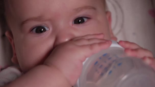 Infant, childhood, emotion concept - Extreme close-up of smiling face of brown-eyed newborn awake toothless baby 7 months old drink water from bottle with nipple lying in white bodysuit in stroller — Stock Video