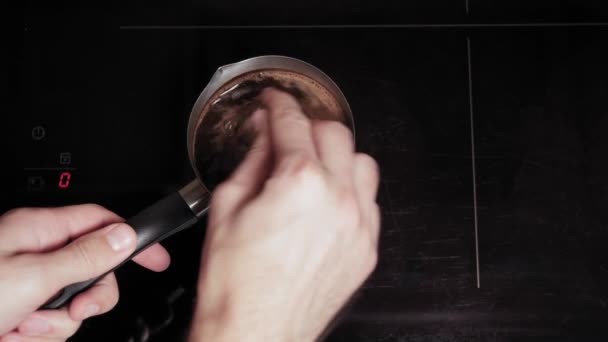 Cafés y restaurantes, desayuno, cocina, concepto de adicción - Primer plano de la mano masculina hacer café en la estufa de cerámica de inducción en acero inoxidable de metal turco. paso 3: remover la bebida con cuchara y espuma — Vídeo de stock