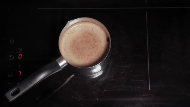 카페와 레스토랑, 아침 식사, 요리, 중독 개념 - 남성 손의 근접 사진이 금속 터크에 있는 유도 세라믹 스토브에서 커피를 만든다. 4 단계: 온도 감소, 원 안에서의 두꺼운 거품 운동 — 비디오