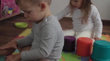 Çocukluk, aile, izolasyon konsepti. Grup iki küçük çocuk yerde oturan büyük parçalardan yumuşak bulmacalar topluyor. Çocuklar. Erkek ve kız kardeş evde motor becerileri için eğitim oyunları oynuyorlar.