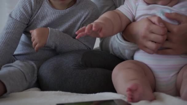 Jeugd, moederschap, broers en zussen concept - zorgeloze jonge moeder horloge cartoons met kleine kinderen, zoon pasgeboren baby hebben plezier spelen op bed, gelukkig vrolijke grote familie lachen kietelt, kus, knuffels liggen ontspannen. — Stockvideo