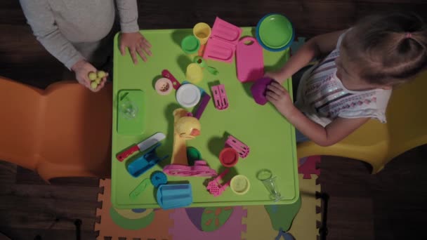 Medicin, familj, spel, barndom, konst koncept - top view glada barn leker med färgad plast glass fabrik sitter vid bordet hemma under karantän. Barn syskon har kul studera tillsammans — Stockvideo