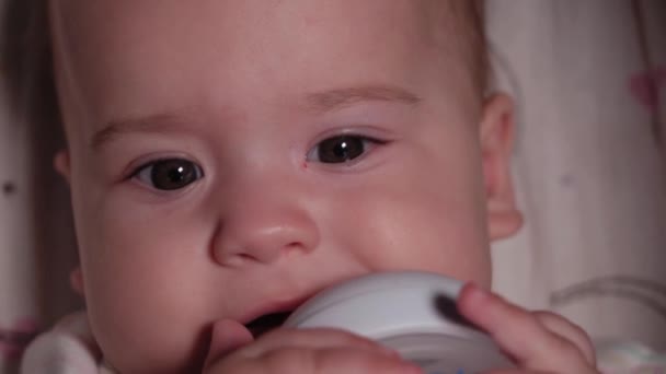 Bambino, infanzia, concetto di emozione - Primo piano estremo del viso sorridente del neonato dagli occhi marroni sveglio senza denti bambino di 7 mesi bere acqua dalla bottiglia con capezzolo sdraiato in body bianco nel passeggino — Video Stock