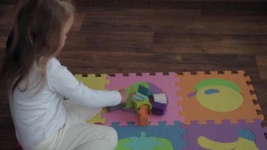 Çocukluk, aile, izolasyon konsepti. Küçük, şirin bir çocuk yerde renkli yumuşak bir yapboz üzerine ahşap piramit inşa ediyor. Küçük kız evde motor becerileri için tek başına eğitim oyunları oynuyor..