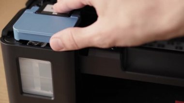 Video talimatları, teknoloji, medya, ofis, kırtasiye konsepti - erkek ellerinin yeni mürekkep püskürtme yazıcıyı fırlatmaya hazırladığı yakın plan. Adım 8: Mürekkep dök - mavi tank kapağını aç ve siyah kapağı çıkar