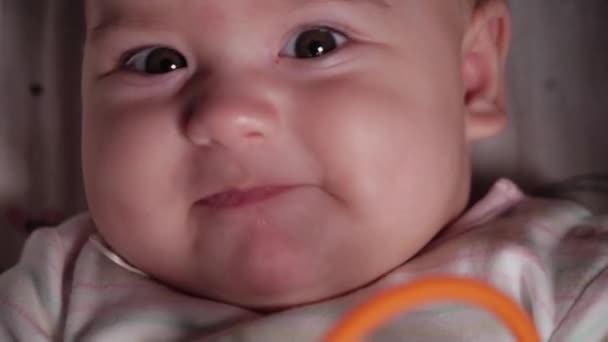 Bebé, infancia, concepto de emoción - Primer plano extremo de la cara sonriente de ojos marrones gordito recién nacido despierto bebé sin dientes 7 meses de edad mirando a la cámara tumbado en traje de cuerpo blanco en el cochecito. Enfoque suave — Vídeos de Stock