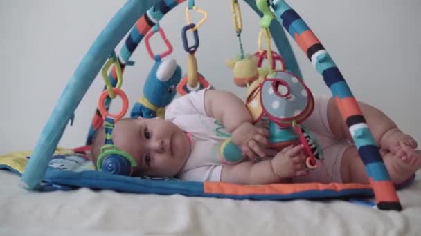 Infancy, childhood, development, health improvement, lifestyle concept - Close up of happy cute newborn kid 5-8 month of age laying on developing mat Activity Gym baby doing tummy time with toy inside — Stock Video