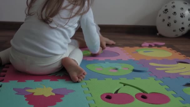 어린 시절, 가족, 절연 개념 - 두 명의 어린 자녀가 바닥에 앉아 있는 커다란 부분의 부드러운 퍼즐 열매를 모은다. 어린이와 자매가 집에서 운동 기술을 배우기 위해 교육용 게임을 하는 모습 — 비디오