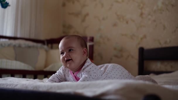 유아, 소아, 부모, 발달, 의학과 건강 개념 - 전면에 보이는 아기 뚱뚱 한 얼굴을 하고 있는 아기 배에 누워 있는 다양 한 색상의 장난감과 함께 웃는 분홍색 보육 복을 입은 행복 한 아기 — 비디오