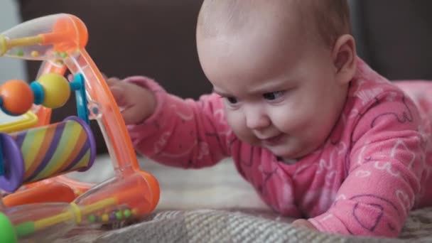 Säuglingsalter, Kindheit, Elternschaft, Entwicklung, Medizin und Gesundheitskonzept - Vorderansicht Großaufnahme pummeliges Neugeborenes fröhliches Wachsein im rosafarbenen Body lächelnd mit buntem Spielzeug auf Bauch liegend — Stockvideo
