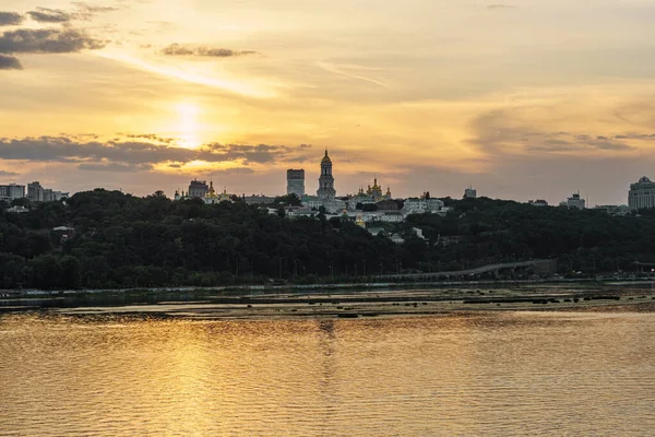 Turism, sevärdheter, historiska, kristendom koncept - antenn utsikt över stranden av floden Dnepr i Kiev och gamla kloster byggnader Kiev-Pechesk Lavra med vackra moln vid solnedgången på sommaren kväll. — Stockfoto