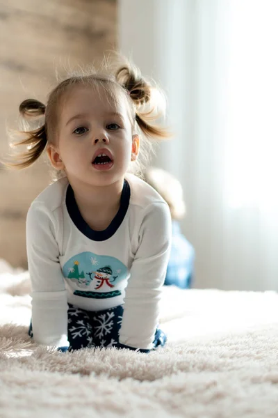 Kindertijd, technologie, baby, kleine concepten - een schattig kind meisje kijken cartoon op de telefoon, smartphone op zacht wit bed in de zonnige kamer. kind in pyjama spreken door video conferentie over gadget binnen — Stockfoto