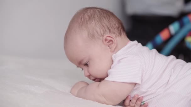 Infância, infância, paternidade, desenvolvimento, medicina e conceito de saúde - visão lateral close-up rosto de bebê recém-nascido gordinho alegre vigília em terno rosa sorrindo e fazendo caretas deitado na barriga — Vídeo de Stock