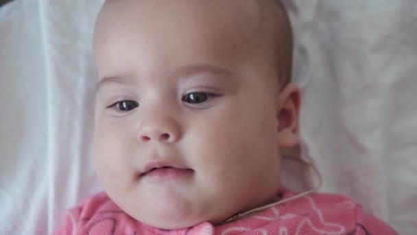 Kindertijd, kindertijd, ouderschap, ontwikkeling, geneeskunde en gezondheid concept - close-up top view gezicht van mollig pasgeboren kalme wakker baby gekleed in roze bodysuit grimaces liggend op rug op witte achtergrond — Stockvideo