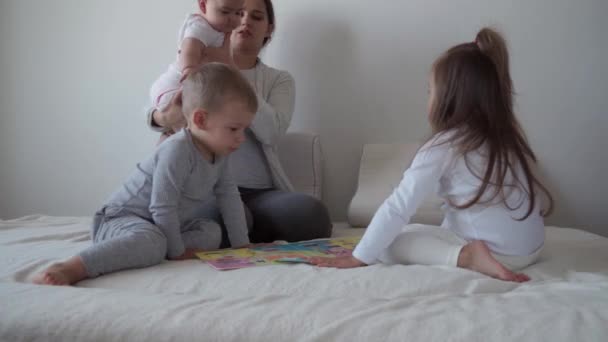 Kindheit, Mutterschaft, Geschwisterkonzept - Unbekümmerte junge Mutter liest Märchen für kleine Kinder, Sohn Neugeborenes hat Spaß beim Spielen im Bett, fröhliches Familienlachen kitzelt, küsst, Umarmungen liegen entspannt — Stockvideo