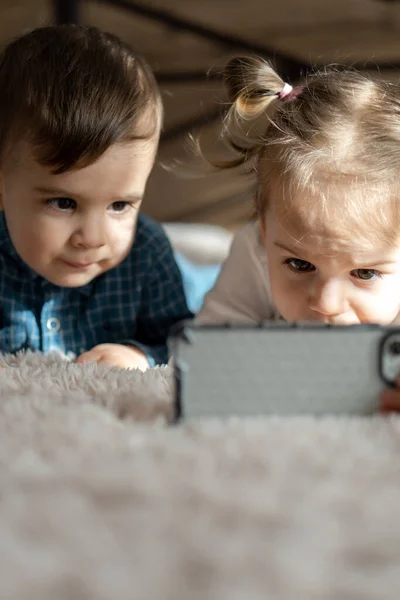Friendship, childhood, technology concepts - 2 young children baby of different nationalities Persian and Slavic appearance watch cartoon on smartphone on bed. kids preschool speak by video conference — Stock Photo, Image